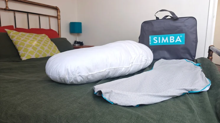 The Simba Body Pillow on a bed, with its cover removed. In the background is the pillow's carry bag