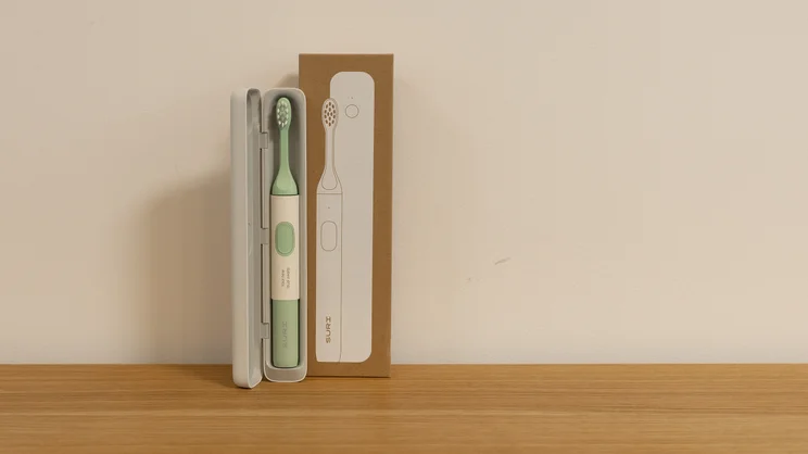 The Suri 2.0 electric toothbrush in its travel case, alongside its box