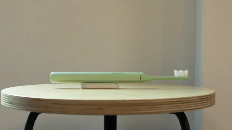 Suri 2.0 electric toothbrush attached to its magnetic mount, lying on a stool