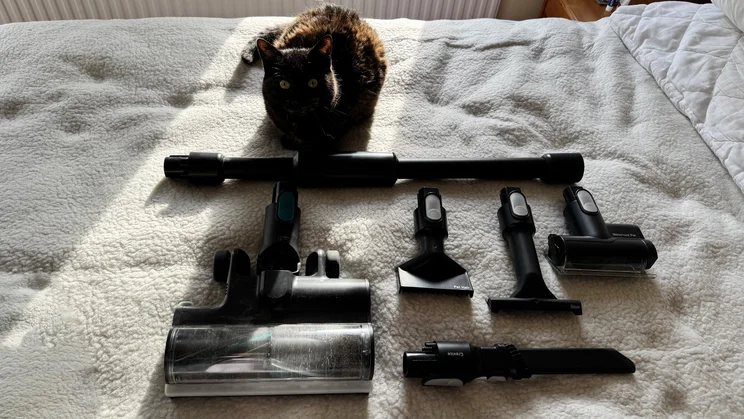 Attachments for the VAX HomePro Detect Pet-Design vacuum cleaner on top of a bed, next to a cat