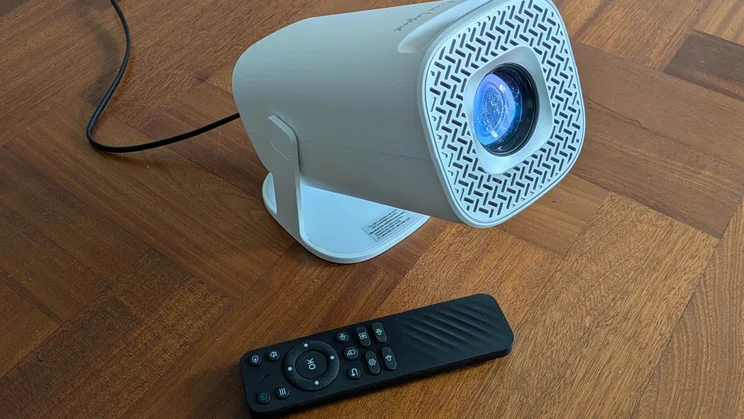 The Acer AOPEN QH15s projector on a wooden floor pointing to the right with its remote control next to its base