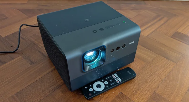 The BenQ GP520 4K projector on a wooden floor with its remote control
