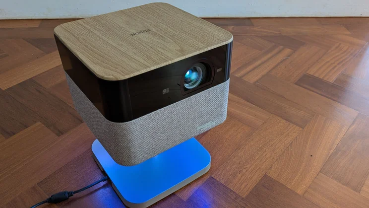 The Epson Lifestudio Flex EF-72 4K projector on a wooden floor with its ambient light coloured blue