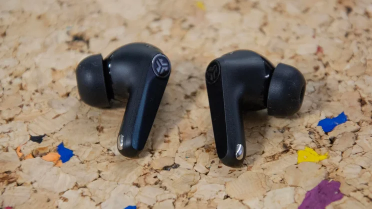The JLab JBuds Pods ANC wireless earbuds on a cork table with their eartips pointing outwards and their stems pointing downwards