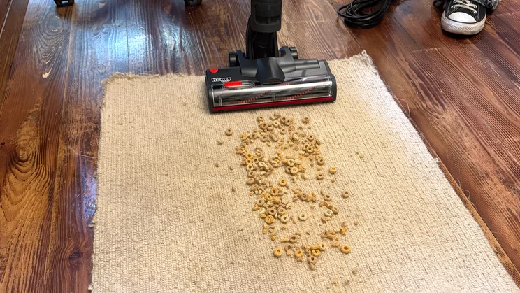 The Henry Quick Corded vacuum cleaner being tested on a square of carpet to pick up Cheerios