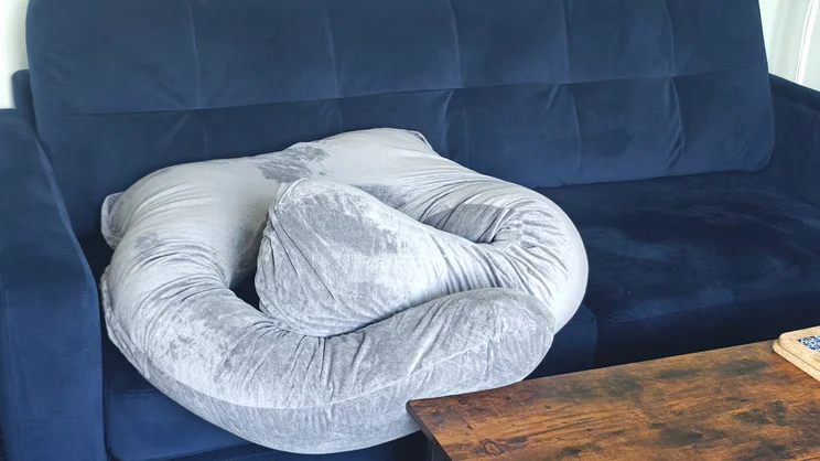 The Nuliie Pregnancy Pillow curled up on a blue sofa