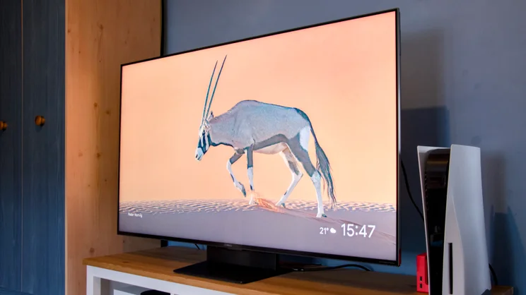 The TCL C7K TV on a cabinet next to a PS5 showing an image of an antelope jumping