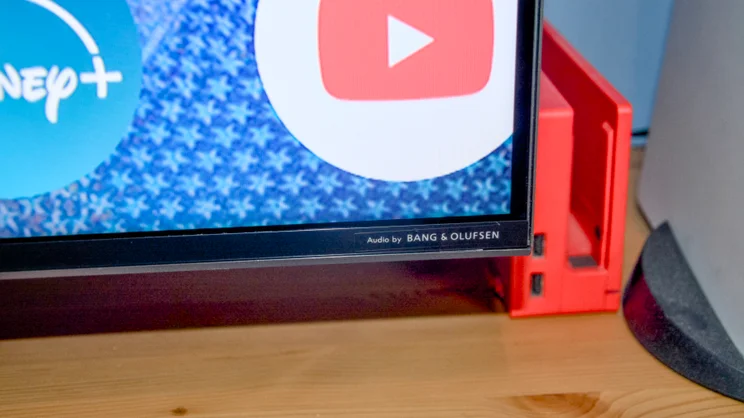 A close up shot of the TCL C7K's Bang & Olufsen audio branding on the bottom left corner of the TV's bezel