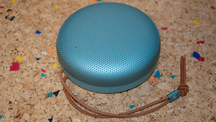 The Bang & Olufsen A1 3rd Gen Bluetooth speaker on a cork table with its leather strap beneath it