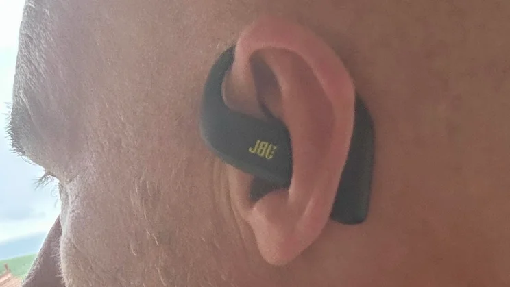 The left earpiece of the JBL Endurance Zone open-ear headphones being worn by a bald man