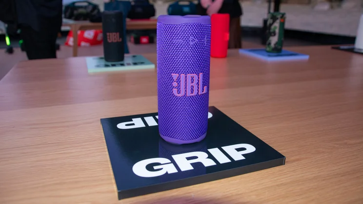 A purple JBL Grip on a table with other Grip speakers in the background