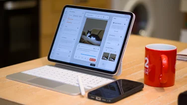 The 11-inch Apple iPad Pro on a maple kitchen table with a cup of coffee and a phone sitting next to it