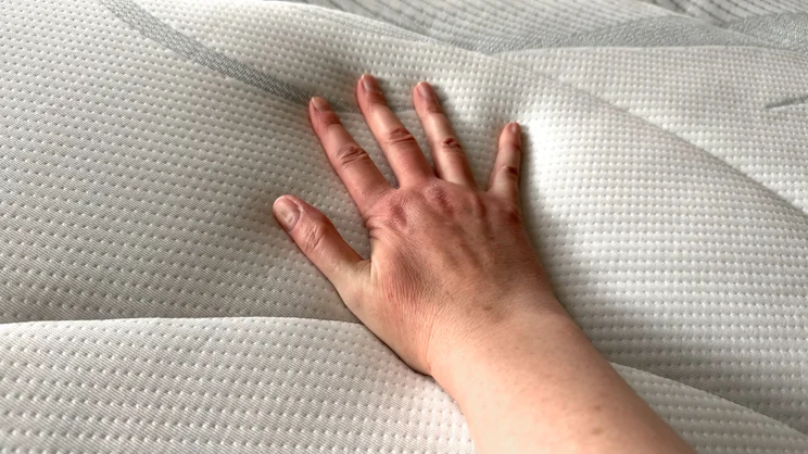 A closeup shot of a hand pushing down on the surface of the Slumberland Air 6.0 Memory mattress