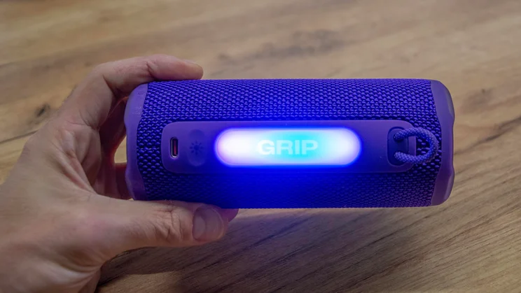 The JBL Grip portable Bluetooth speaker being held horizontally in our reviewer's hand with the ambient light illuminated blue and purple