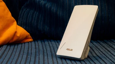 The Asus-RP-BE58 Wi-Fi 7 wireless extender pictured from the front, on a blue and oragen corduroy sofa