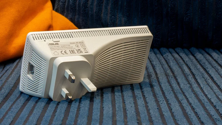 The Asus-RP-BE58 Wi-Fi 7 wireless extender pictured from the rear, on a blue and oragen corduroy sofa
