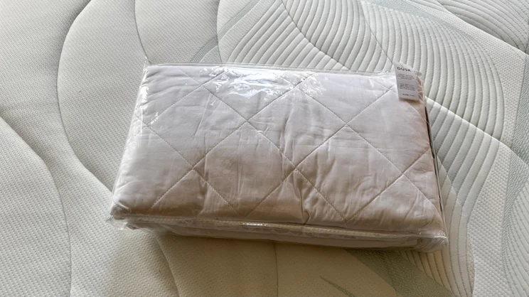 The Dusk Luxury Quilted Mattress Protector in its packaging, on the surface of a mattress
