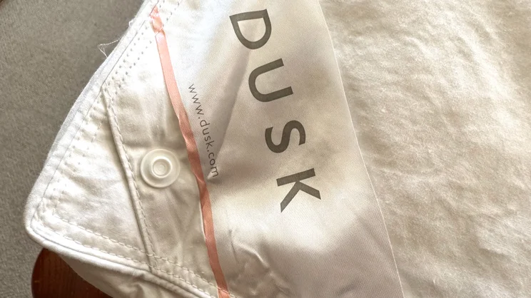 A closeup of the Dusk Supreme Goose Down mattress topper, with a label showing Dusk's logo