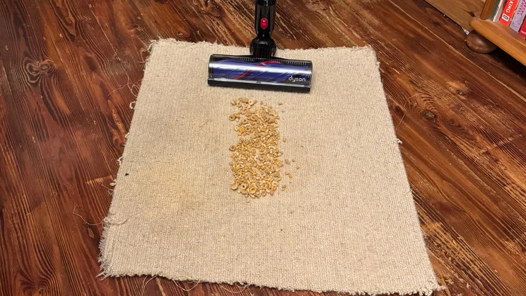 The Dyson V8 Cyclone vacuum cleaner being used to clean Cheerios from a piece of carpet
