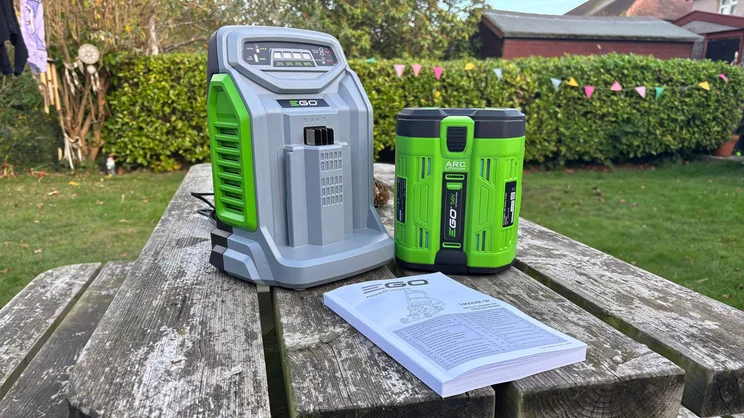 The LM2236E-SP lawn mower's battery, charger and instruction manual on a garden table