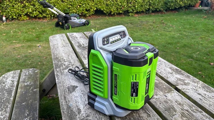 The LM2236E-SP lawn mower's battery and charger on a garden table