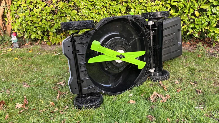 The LM2236E-SP lawn mower on a lawn in front of a hedge. The mower is tipped on its side, showing its blades