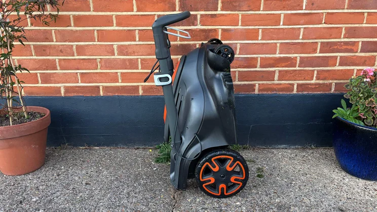 A side view of the Flymo 36V Ultramow 460 Duo, folded against a brick wall