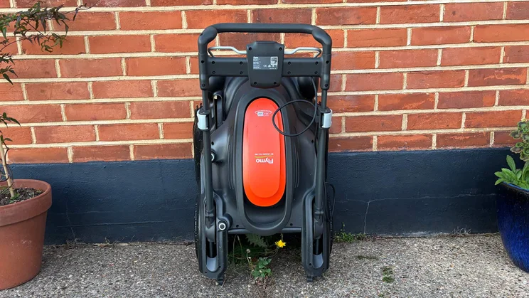 The Flymo 36V Ultramow 460 Duo folded, against a brick wall