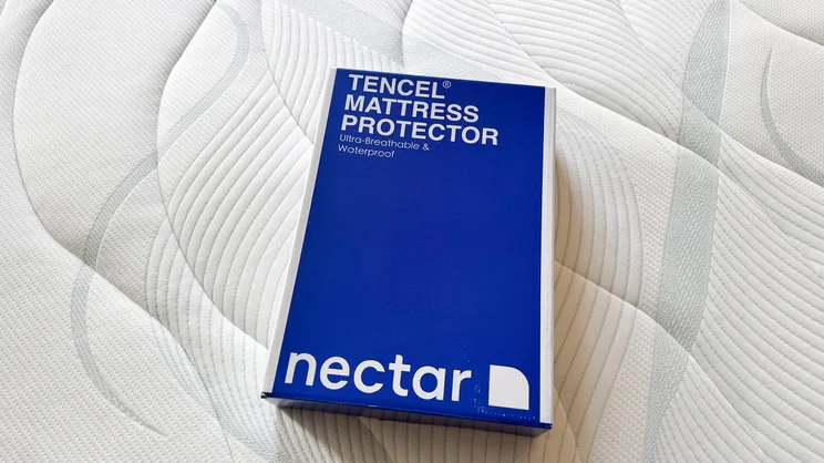The Nectar mattress protector in its packaging, on the surface of a mattress