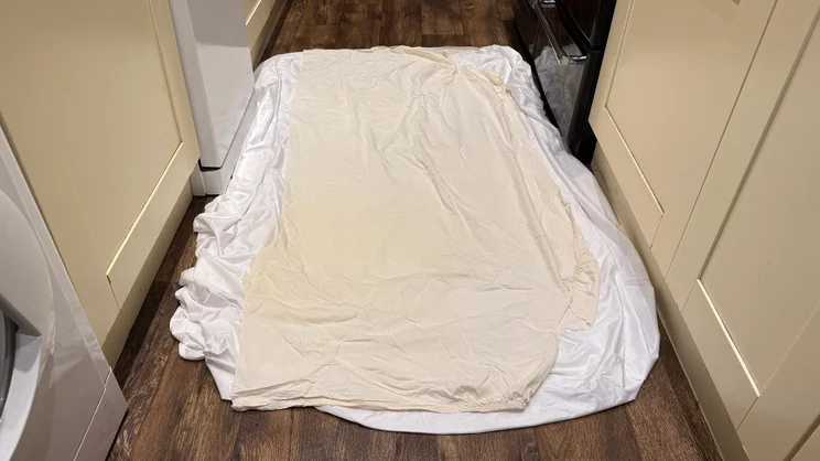 The Nectar mattress protector on the floor, with a polycotton sheet covering it