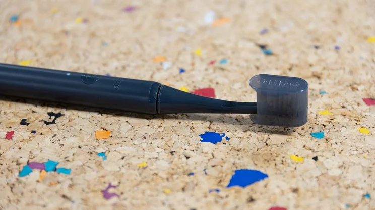 The Ordo Sonic Edge toothbrush, with travel cap on, laid down on a multicoloured cork table