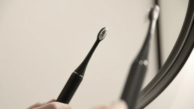 The Ordo Sonic Edge toothbrush in a hand, reflected in a bathroom mirror