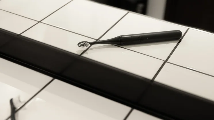 The Ordo Sonic Edge toothbrush laid flat on tiles, reflected in a bathroom mirror
