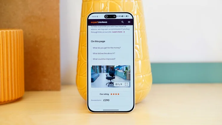 Poco F8 Pro leaning against a vase, showing the Expert Reviews homepage on the display
