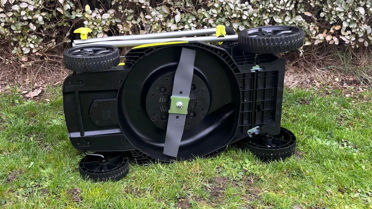 The Ryobi RY18LMX33A lawn mower tipped on its side, showing the blades