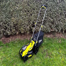 The Ryobi RY18LMX33A lawn mower on a lawn in front of a hedge