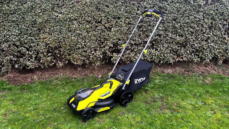 The Ryobi RY18LMX33A lawn mower on a lawn in front of a hedge