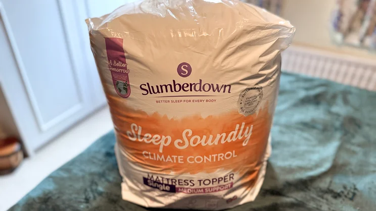 The Slumberdown Sleep Soundly Climate Control mattress topper in its packaging, on a bed