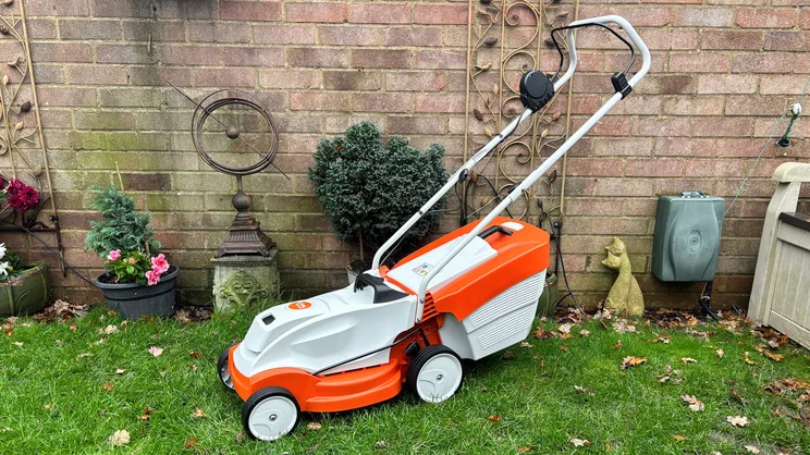 The Stihl RMA 235 lawn mower in a garden, in front of a brick wall