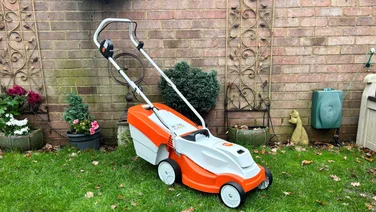 The Stihl RMA 235 lawn mower in a garden, in front of a brick wall