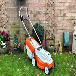 The Stihl RMA 235 lawn mower in a garden, in front of a brick wall