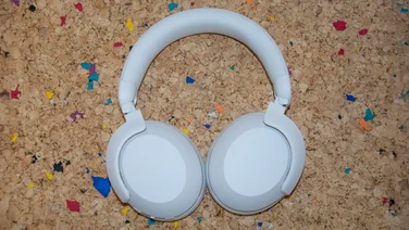 The Philips H8000E over-ear headphones laid earcups down on a cork table