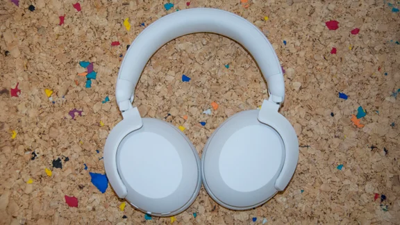 The Philips H8000E over-ear headphones laid earcups down on a cork table