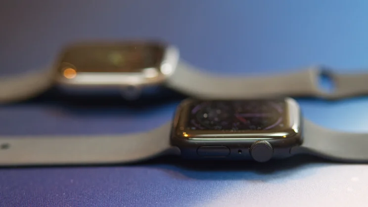 Apple Watch SE 3 lying flat on a blue and white mat with the Apple Watch Series 11 in the background