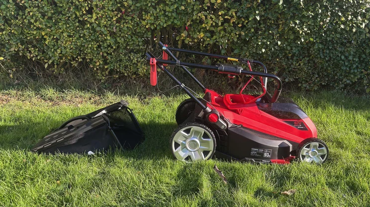 The Cobra MX4340VX lawn mower on a lawn in front of a hedge, with its grass collector removed and placed behind it