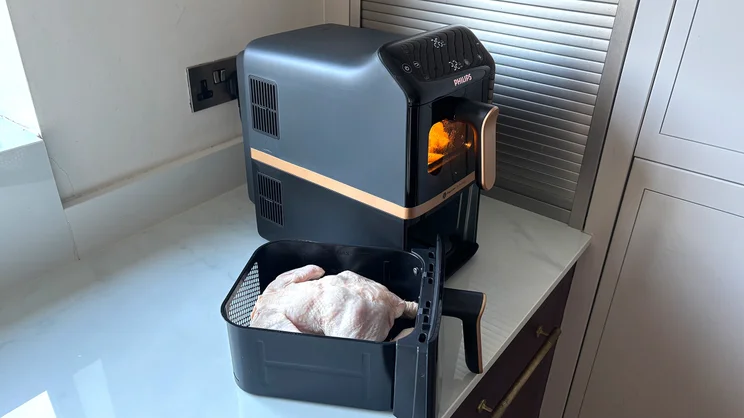 Chips cooking in the top drawer of the Philips 4000 Series Stacked Dual Basket Air Fryer while a raw chicken sits in the bottom drawer, which has been removed