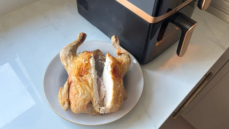 Viewed from above, a halved cooked chicken on a plate, next to the Philips 4000 Series Stacked Dual Basket Air Fryer on a kitchen worktop