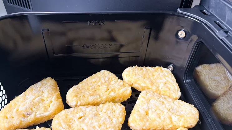 A close up of raw hash browns in a basket of the Philips 4000 Series Stacked Dual Basket Air Fryer
