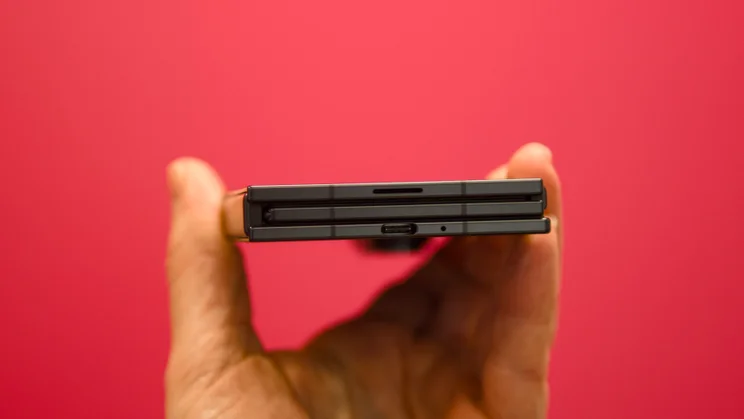 The Samsung Galaxy Z TriFold, folded, pictured from the bottom edge against a pink background