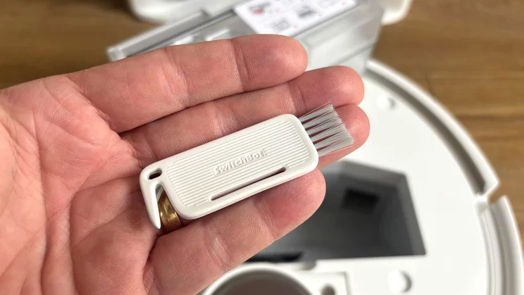 A hand holding a small brush tool for the Switchbot S20 robot vacuum